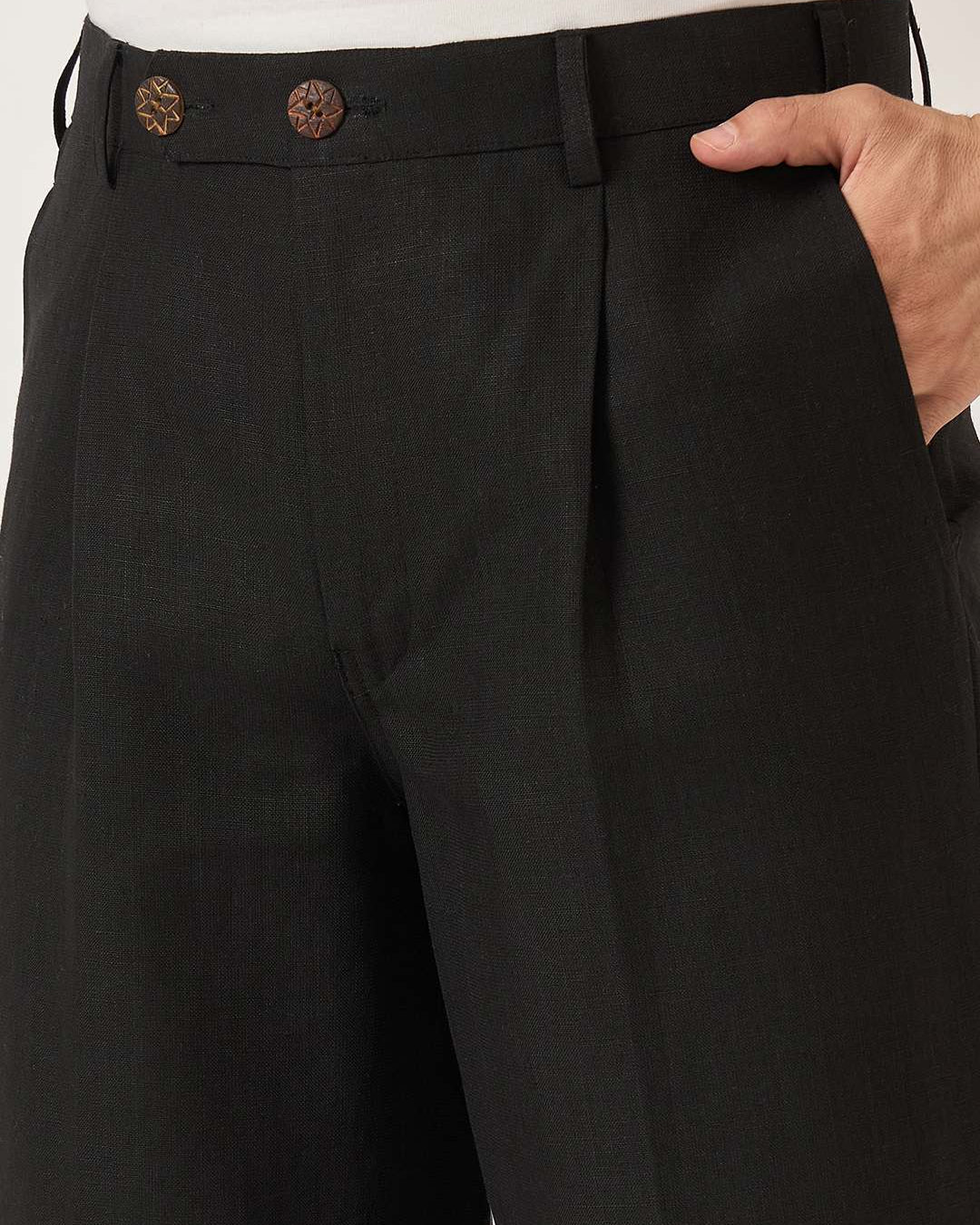 Black pleated pants with brown buttons worn by a person.