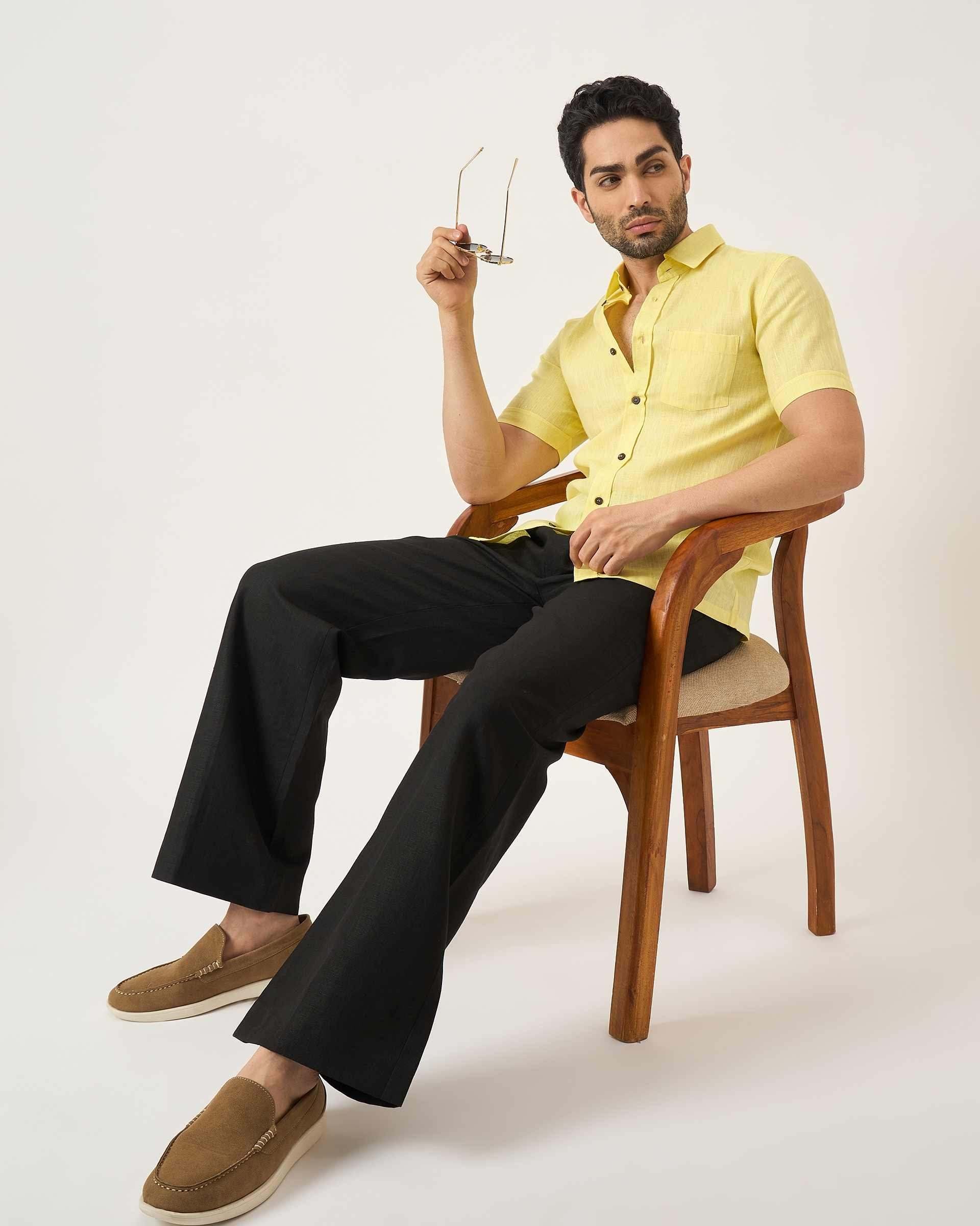 Man sitting on a chair wearing a yellow shirt and black pants.