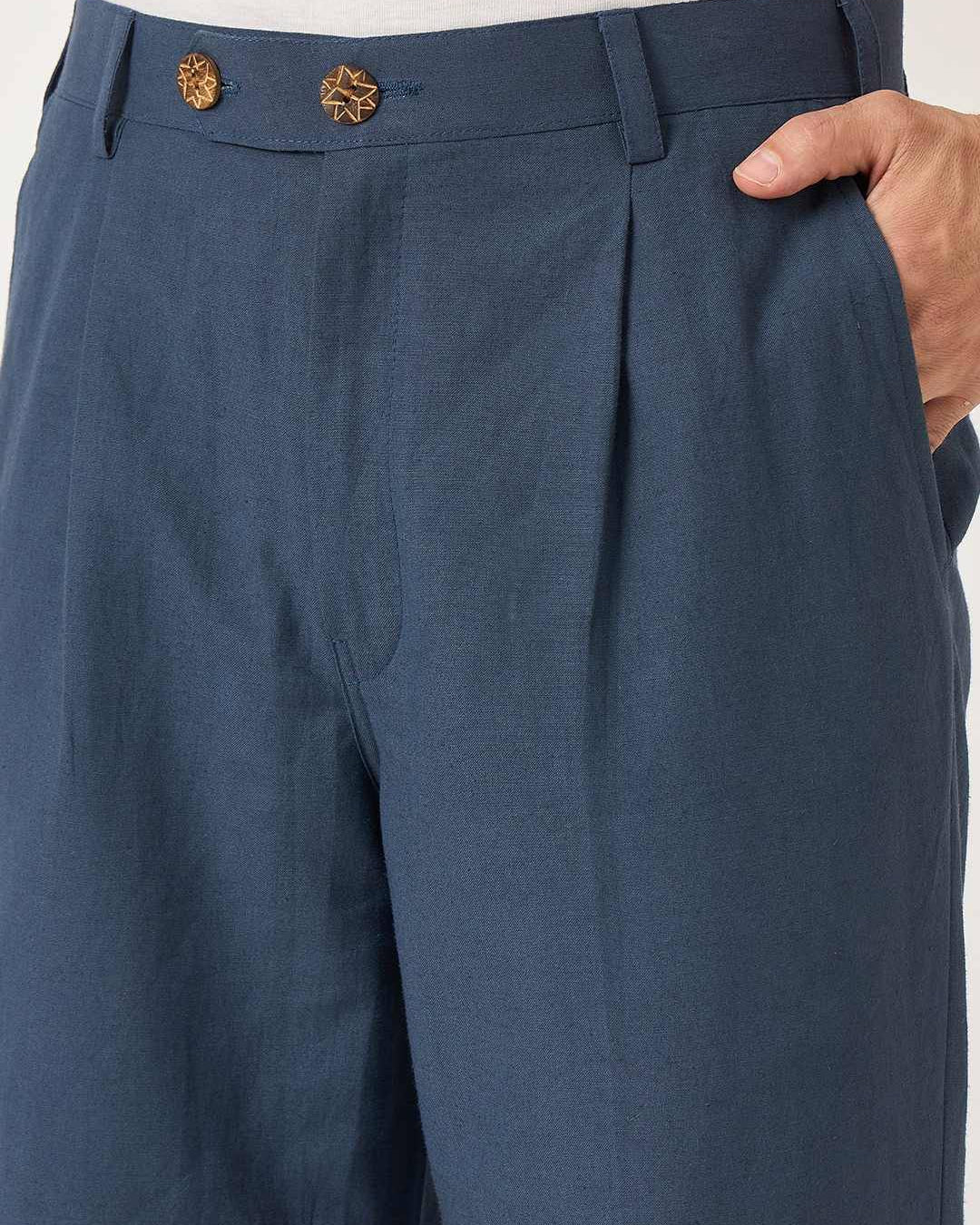 Blue pleated pants with a hand adjusting the waistband on a white background