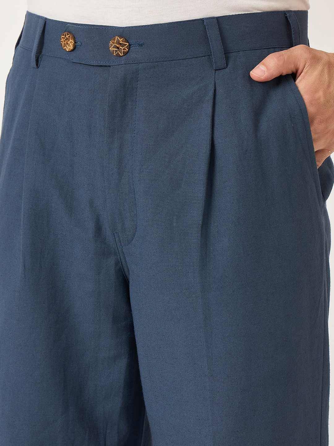 Blue pleated pants with a hand adjusting the waistband on a white background