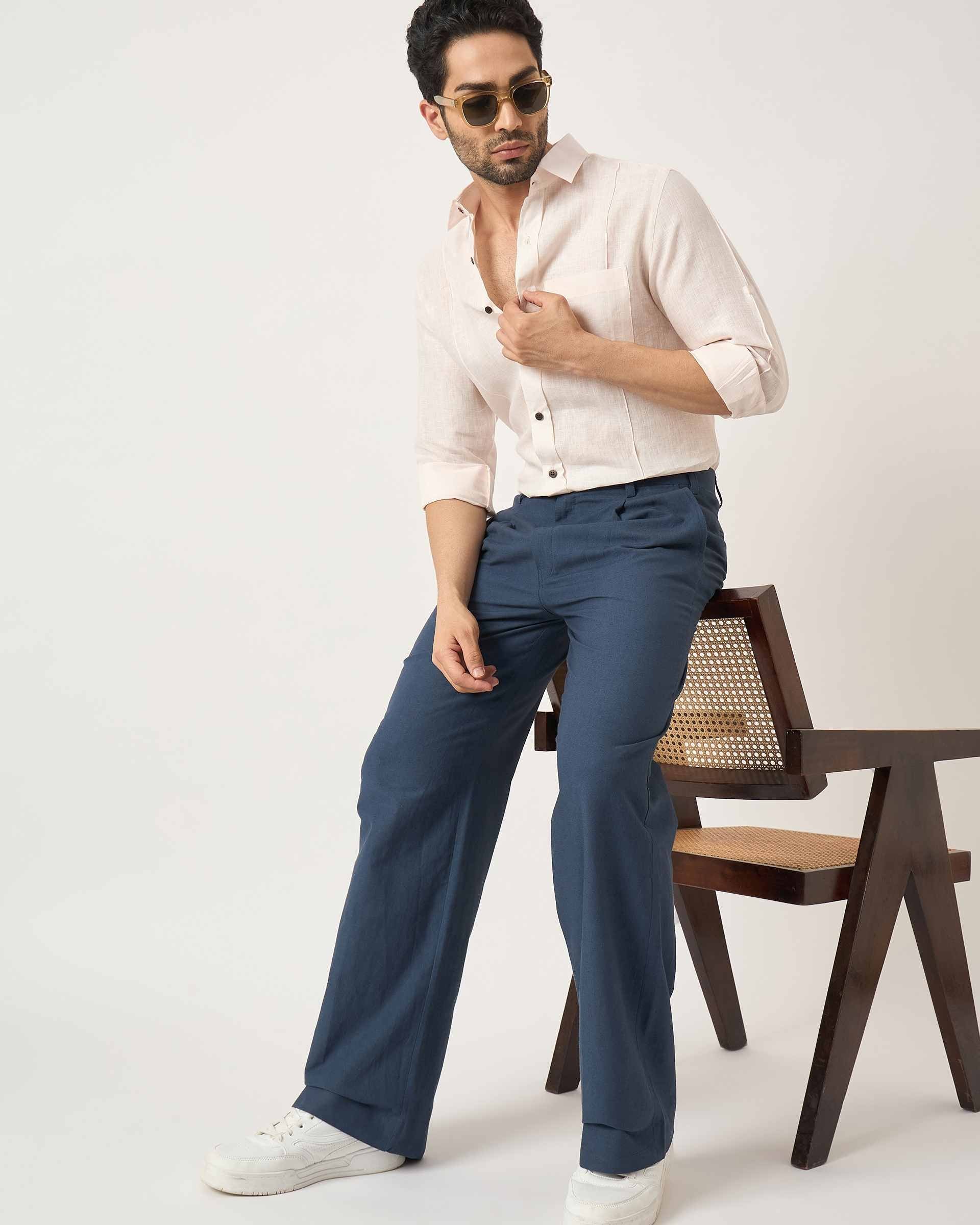 Man wearing a white shirt and blue pants sitting on a chair against a plain background