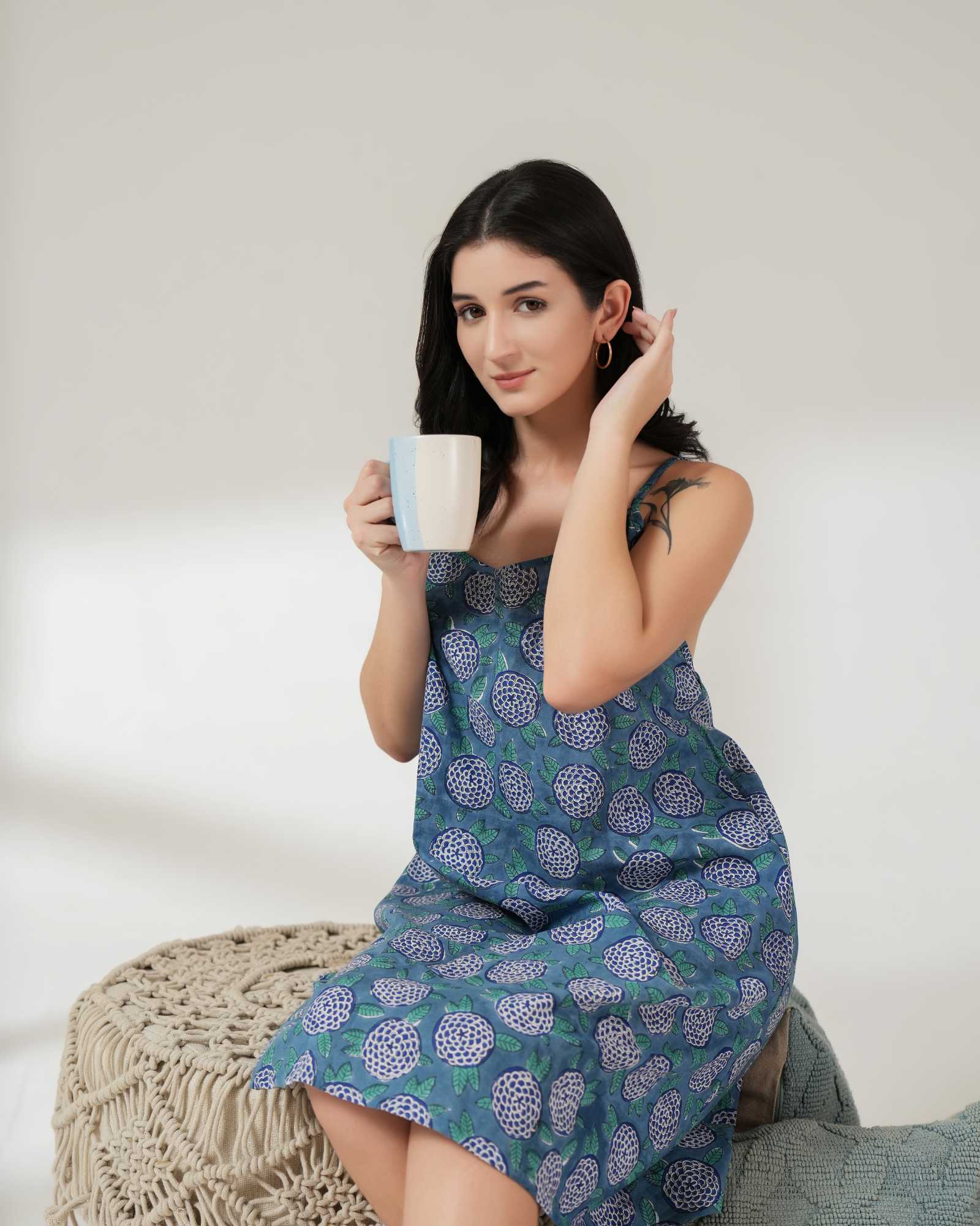Woman in a patterned dress holding a mug against a neutral background