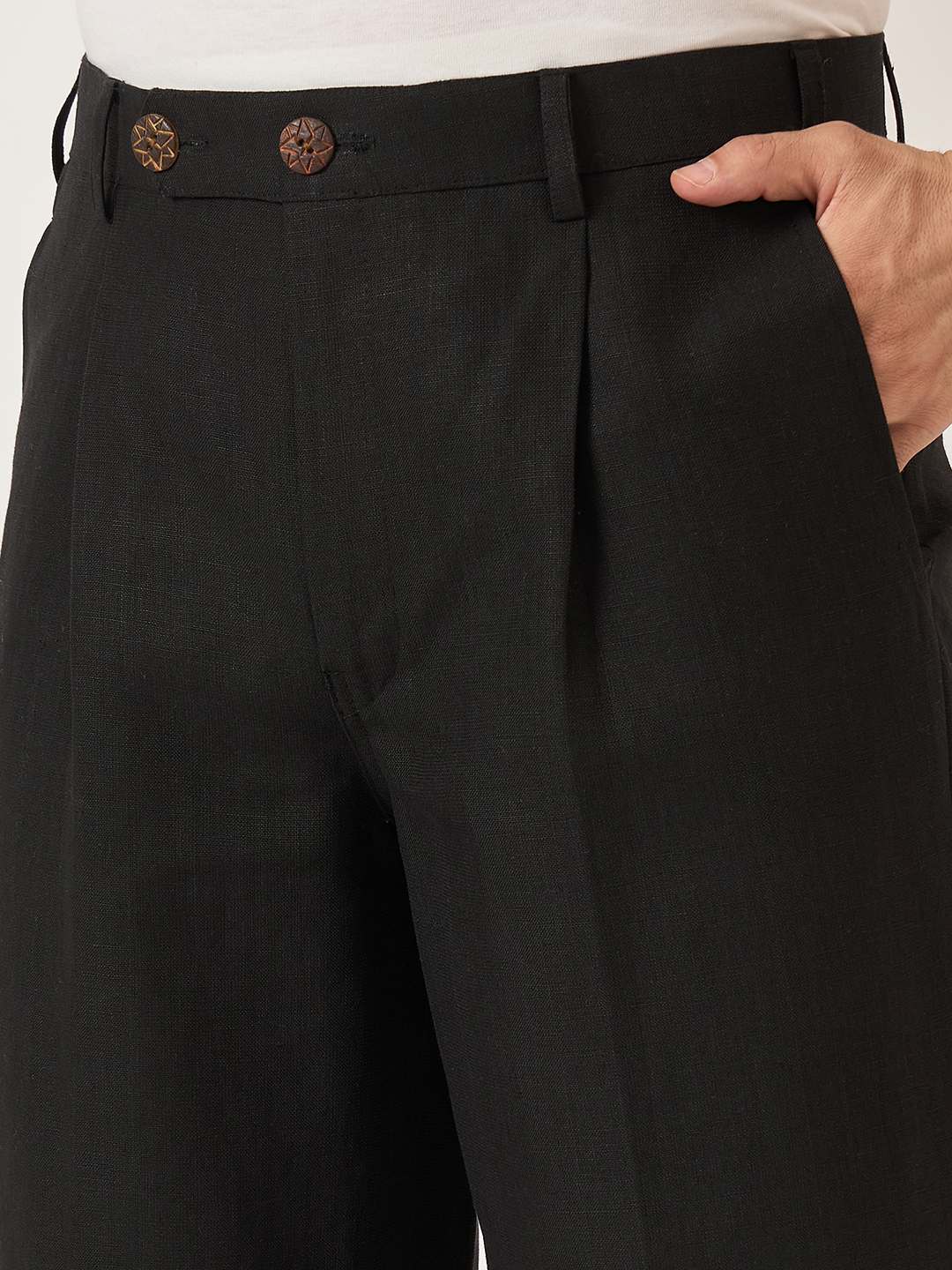 Black pleated pants with brown buttons worn by a person.