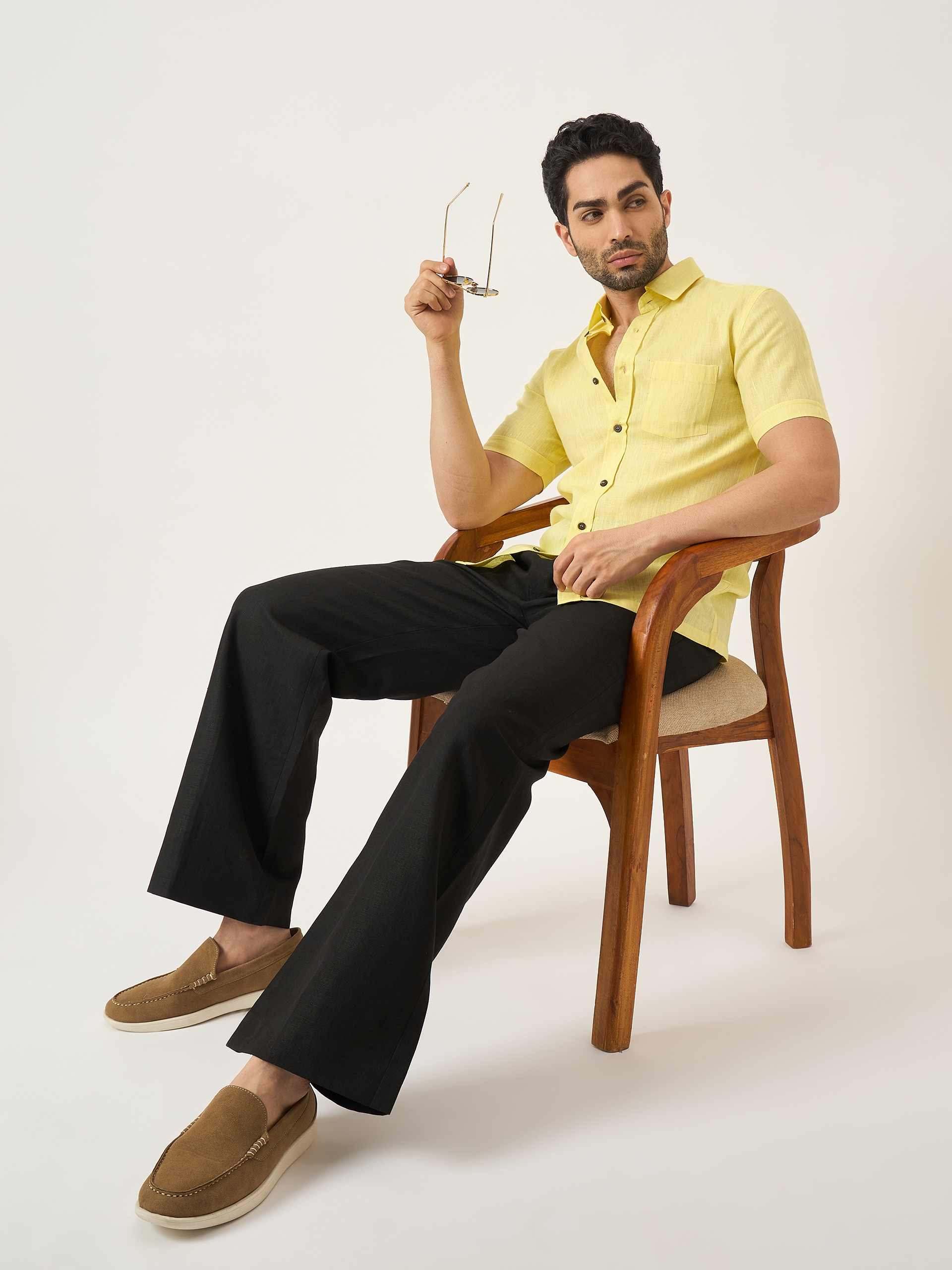 Man sitting on a chair wearing a yellow shirt and black pants.