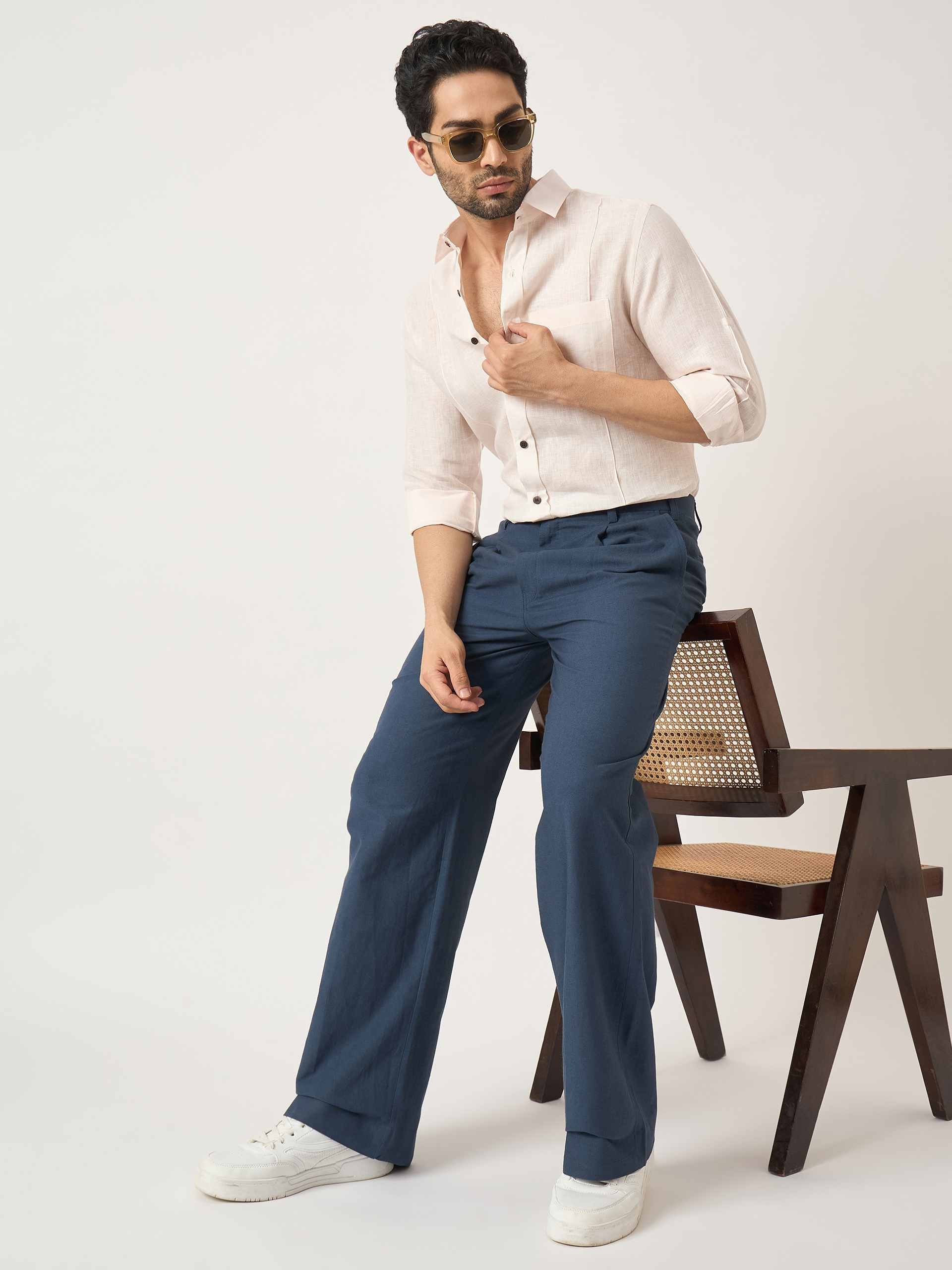 Man wearing a white shirt and blue pants sitting on a chair against a plain background