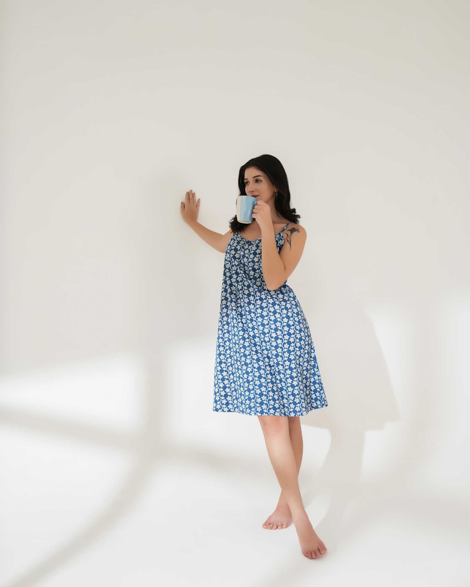 Woman wearing a blue floral dress holding a mug against a white background