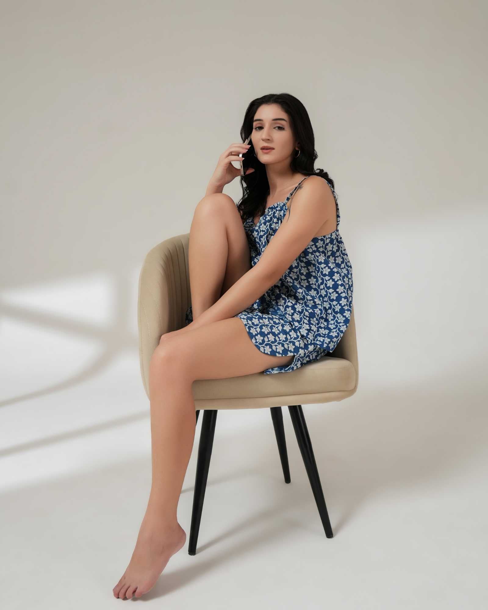 Woman in a blue floral dress sitting on a chair against a white background