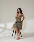 Woman sitting on a chair wearing a colorful patterned dress against a white background