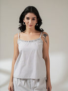 A woman modeling a white and gray vertically striped camisole top with ruffled straps, paired with matching light gray pants, against a neutral beige studio background.